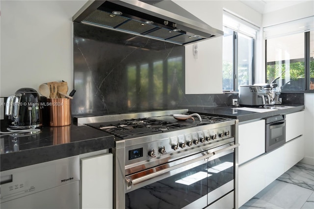 kitchen featuring light tile patterned flooring, tasteful backsplash, wall chimney range hood, range with two ovens, and oven