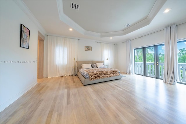 bedroom with multiple windows, light wood-type flooring, a raised ceiling, and access to outside