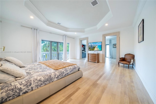 bedroom featuring crown molding, a raised ceiling, light hardwood / wood-style floors, and access to outside