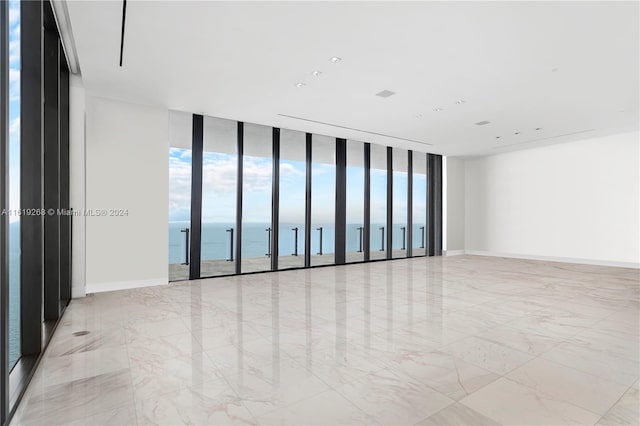 empty room featuring a wall of windows, marble finish floor, a water view, and baseboards