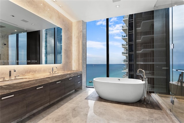 bathroom with double vanity, a water view, a freestanding bath, a sink, and a wall of windows