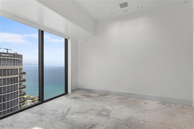 empty room with marble finish floor, a water view, and baseboards