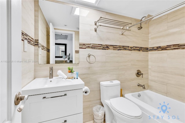 full bathroom with toilet, tiled shower / bath, vanity, tile walls, and a skylight