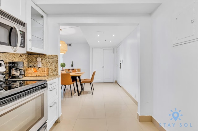 kitchen with light tile patterned floors, backsplash, stainless steel appliances, white cabinets, and electric panel