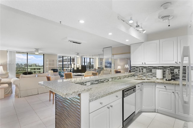 kitchen featuring dishwashing machine, white cabinets, tasteful backsplash, kitchen peninsula, and light stone counters