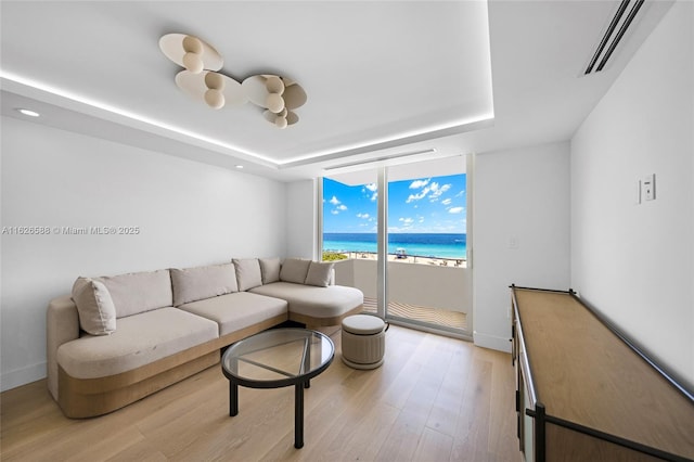 living area featuring light wood-type flooring, visible vents, a water view, floor to ceiling windows, and a raised ceiling