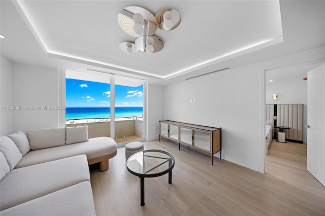 living area featuring a raised ceiling, wood finished floors, a water view, and visible vents