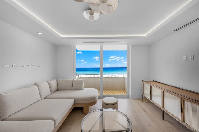 living room featuring a view of the beach, a raised ceiling, light wood-style floors, and a water view