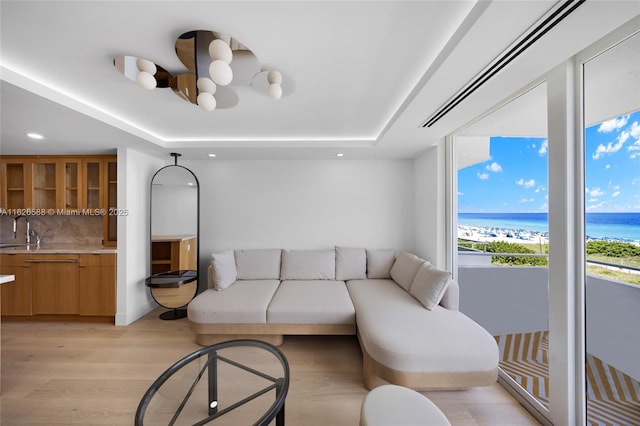 living room with recessed lighting, a raised ceiling, light wood-style floors, and a water view