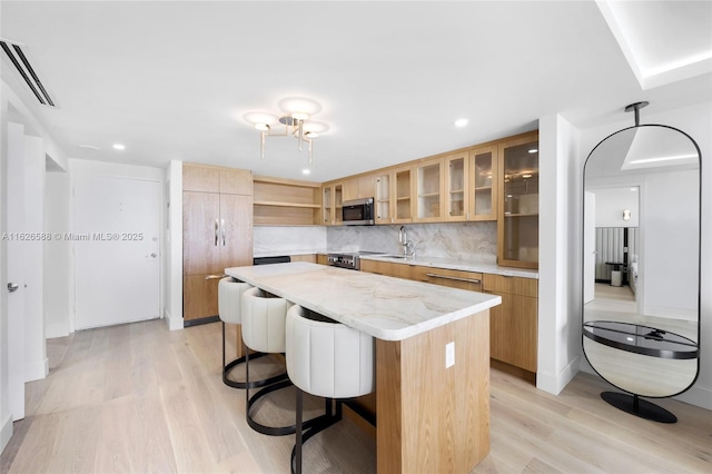 kitchen with a breakfast bar area, open shelves, stainless steel microwave, light wood-type flooring, and a center island