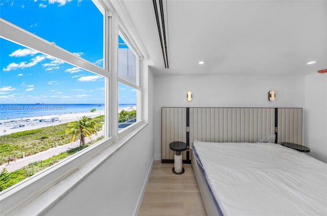 bedroom with a water view, light wood-style flooring, a beach view, recessed lighting, and baseboards