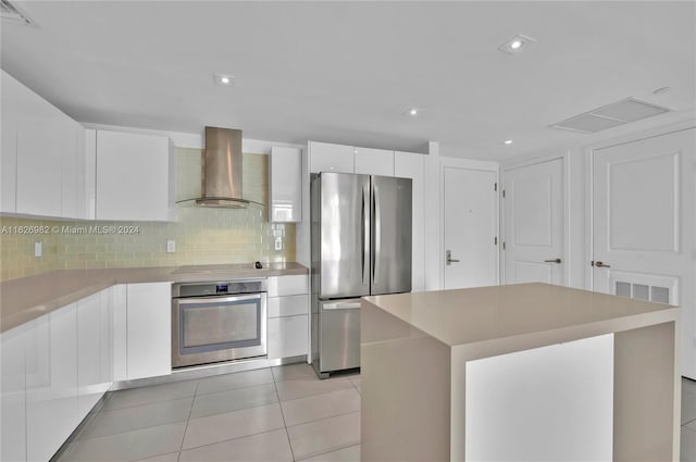 kitchen featuring appliances with stainless steel finishes, a kitchen island, white cabinetry, wall chimney exhaust hood, and light tile patterned floors