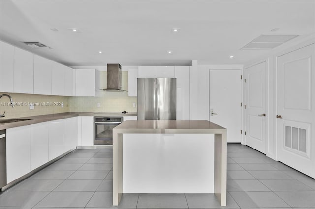 kitchen with a kitchen island, wall chimney exhaust hood, sink, white cabinetry, and appliances with stainless steel finishes