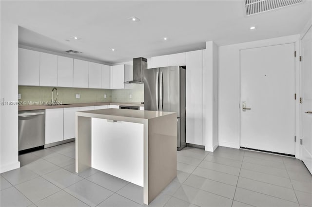 kitchen with a kitchen island, wall chimney range hood, stainless steel appliances, sink, and white cabinetry