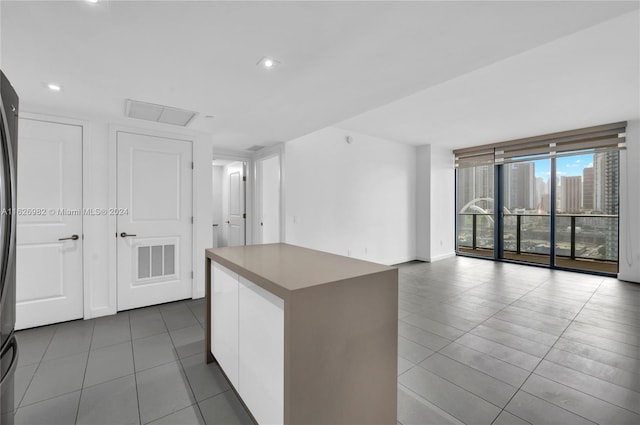 kitchen with dark tile patterned floors, a kitchen island, white cabinets, and a wall of windows