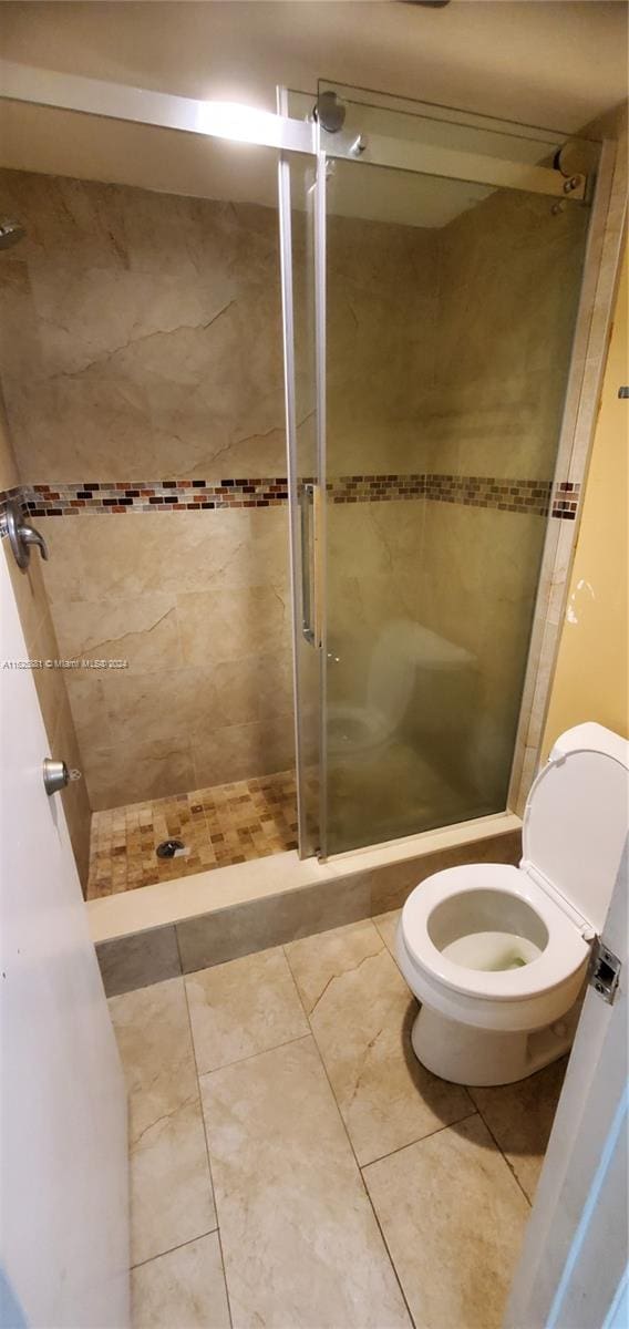 bathroom featuring tile patterned floors, a shower with shower door, and toilet