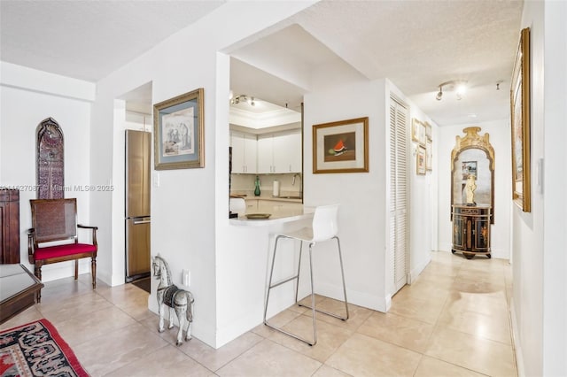 corridor with light tile patterned floors, baseboards, a sink, and a textured ceiling