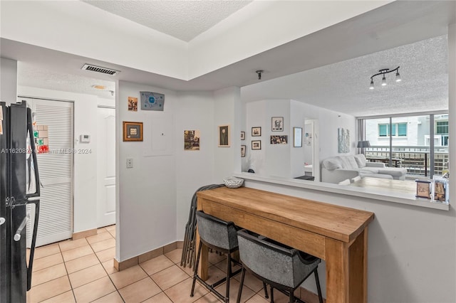 kitchen with black refrigerator, kitchen peninsula, a textured ceiling, and light tile patterned floors