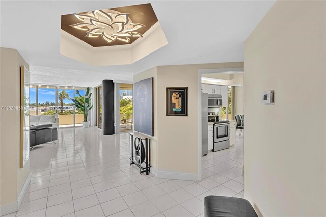 corridor with floor to ceiling windows, a tray ceiling, and light tile patterned floors