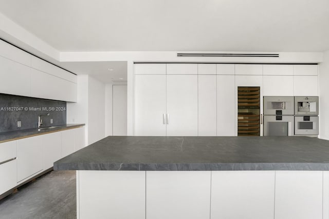 kitchen featuring double oven, tasteful backsplash, and white cabinets