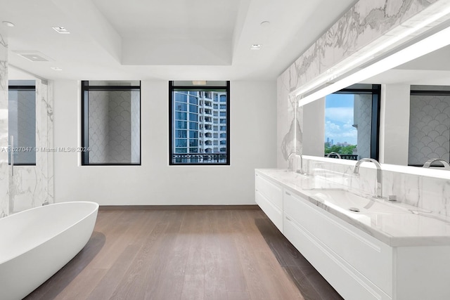 bathroom with hardwood / wood-style flooring, vanity, a bath, and a tray ceiling