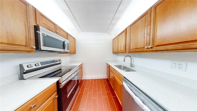 kitchen with sink, appliances with stainless steel finishes, a textured ceiling, and light stone counters