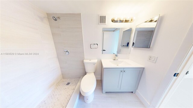 bathroom with vanity, toilet, a tile shower, and tile patterned flooring