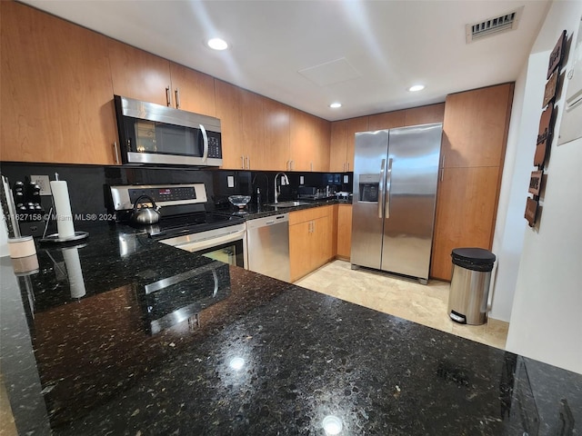 kitchen featuring decorative backsplash, sink, dark stone countertops, appliances with stainless steel finishes, and light tile patterned floors