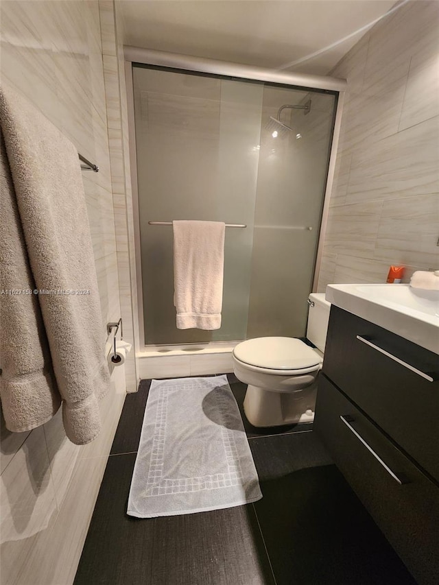 bathroom featuring vanity, toilet, an enclosed shower, and tile walls