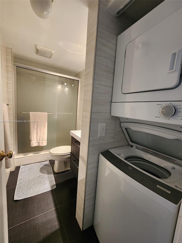 laundry room featuring dark tile patterned flooring and stacked washing maching and dryer