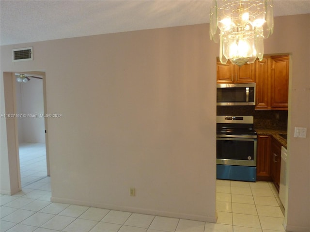 kitchen with light tile patterned floors, stainless steel appliances, visible vents, brown cabinetry, and dark countertops