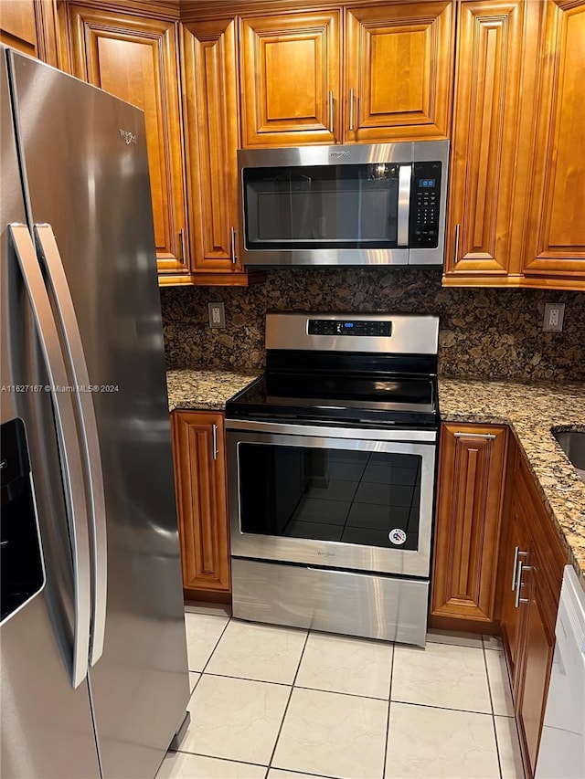 kitchen featuring stainless steel appliances, tasteful backsplash, brown cabinetry, and light stone countertops