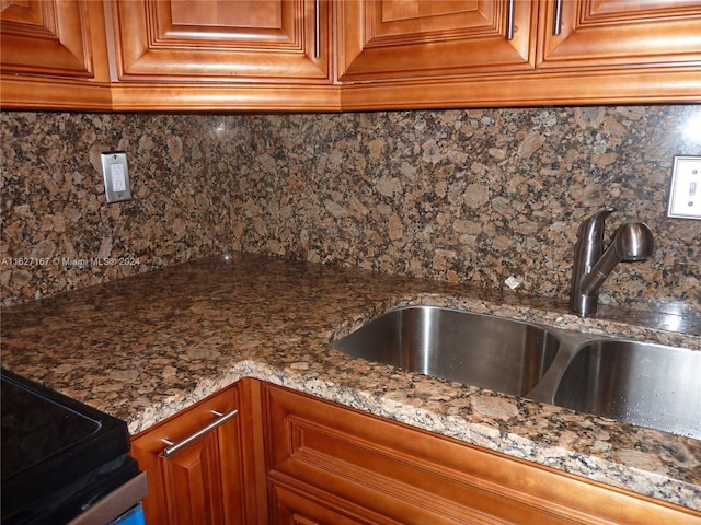 kitchen with brown cabinetry, dark stone counters, a sink, and backsplash