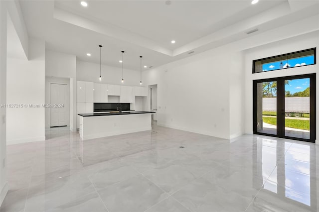 unfurnished living room with french doors, a tray ceiling, sink, and a high ceiling