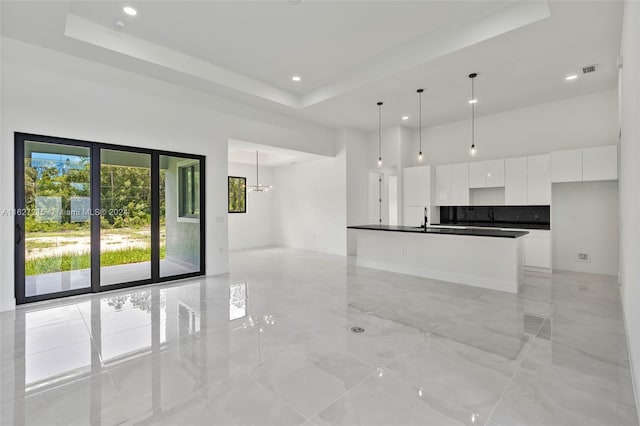 kitchen with sink, white cabinetry, a center island with sink, pendant lighting, and a towering ceiling