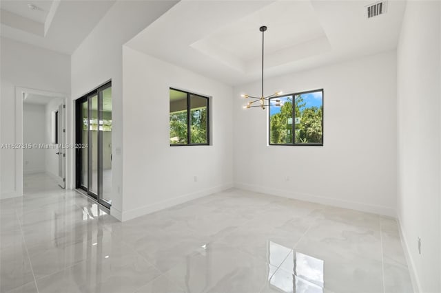 tiled empty room with a chandelier, a raised ceiling, and a wealth of natural light