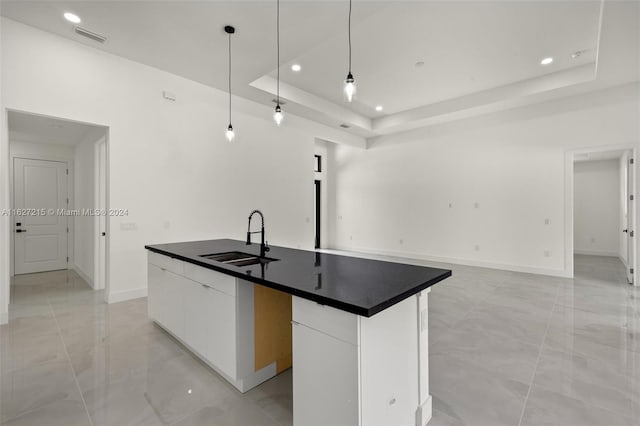 kitchen with white cabinetry, a kitchen island with sink, a tray ceiling, pendant lighting, and sink