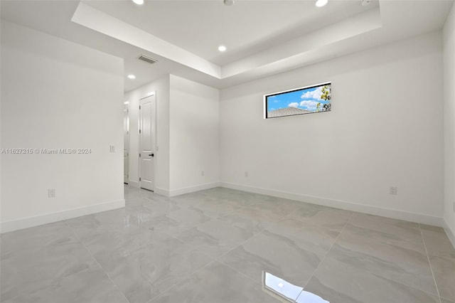 tiled empty room featuring a raised ceiling