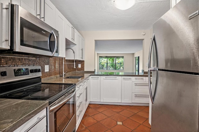 kitchen with dark tile patterned floors, appliances with stainless steel finishes, white cabinetry, backsplash, and dark stone countertops