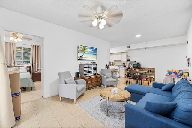 living room featuring ceiling fan, light tile patterned flooring, and a textured ceiling