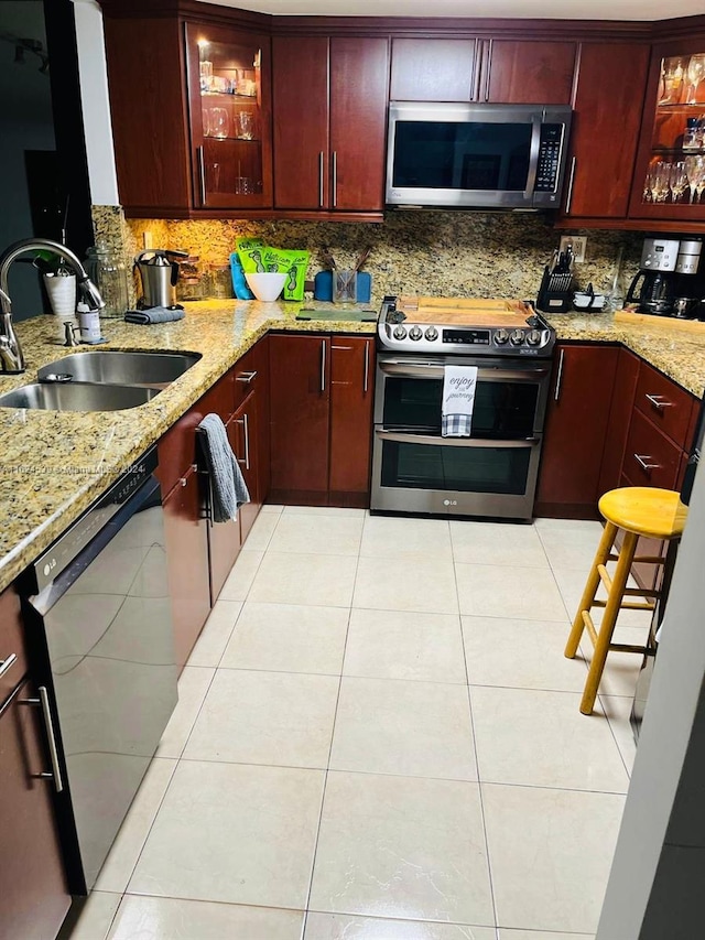 kitchen featuring stainless steel appliances, sink, light stone counters, light tile patterned floors, and decorative backsplash