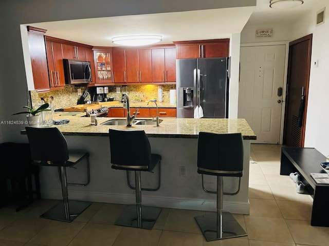 kitchen featuring decorative backsplash, kitchen peninsula, light stone counters, and black fridge