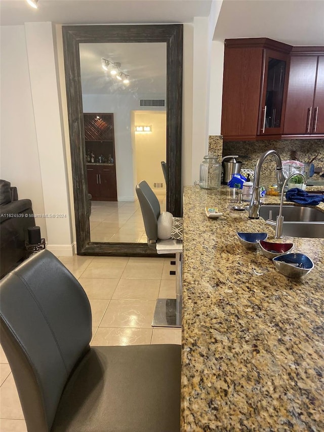 kitchen featuring light tile patterned flooring, backsplash, light stone countertops, and sink