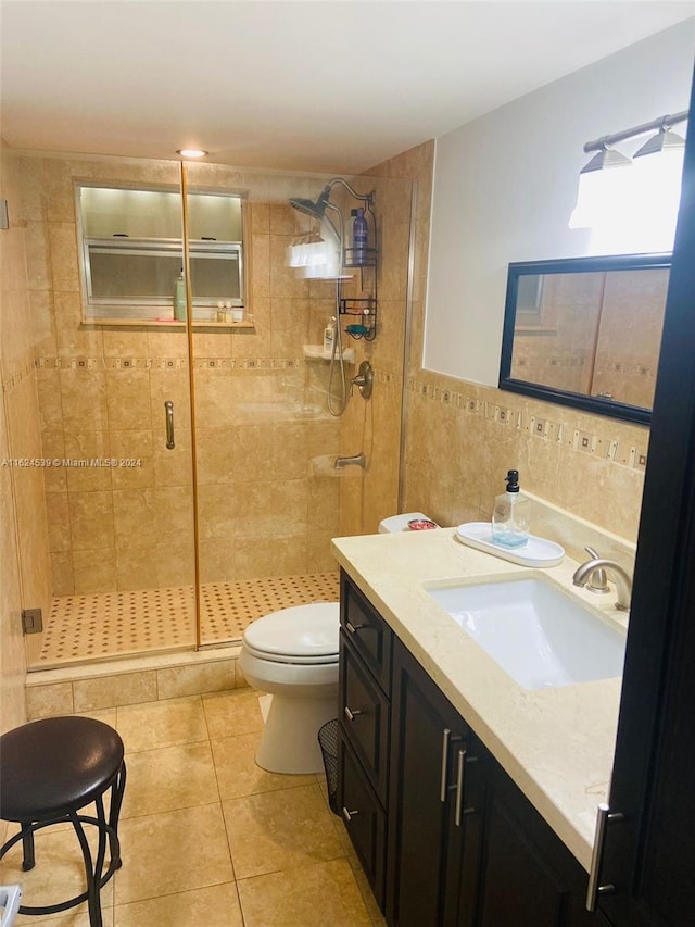 bathroom with vanity, tile patterned floors, tile walls, toilet, and a shower with door