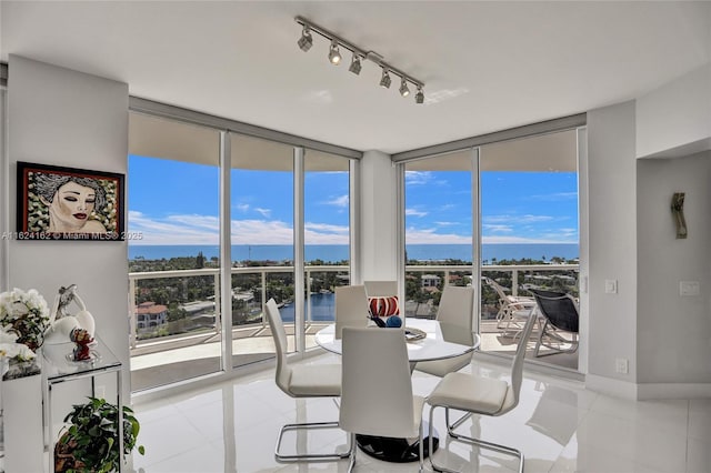 dining room with baseboards, a water view, rail lighting, floor to ceiling windows, and light tile patterned flooring