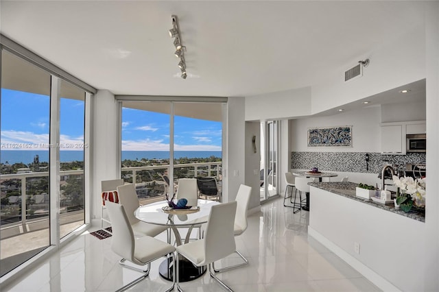 dining room featuring marble finish floor, floor to ceiling windows, rail lighting, a water view, and visible vents