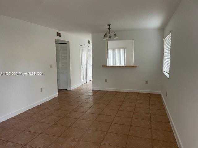 unfurnished room with dark tile patterned flooring and a notable chandelier