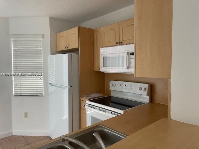 kitchen featuring white appliances, light brown cabinets, a textured ceiling, and light tile patterned flooring