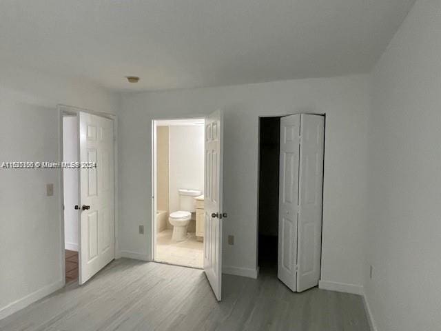 unfurnished bedroom featuring ensuite bath and light wood-type flooring