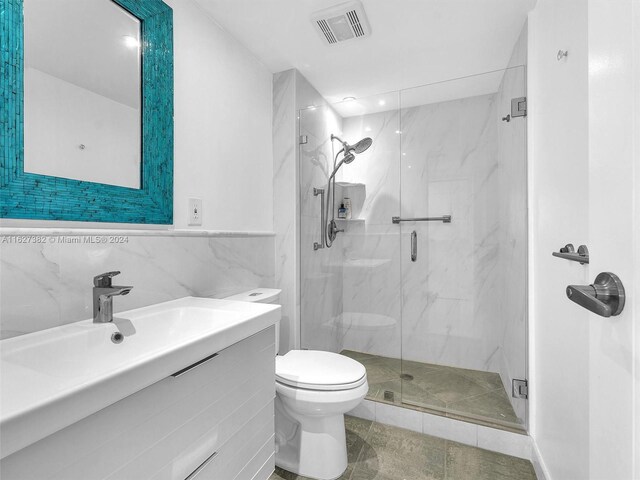 bathroom featuring a shower with shower door, tile walls, tile patterned floors, toilet, and vanity